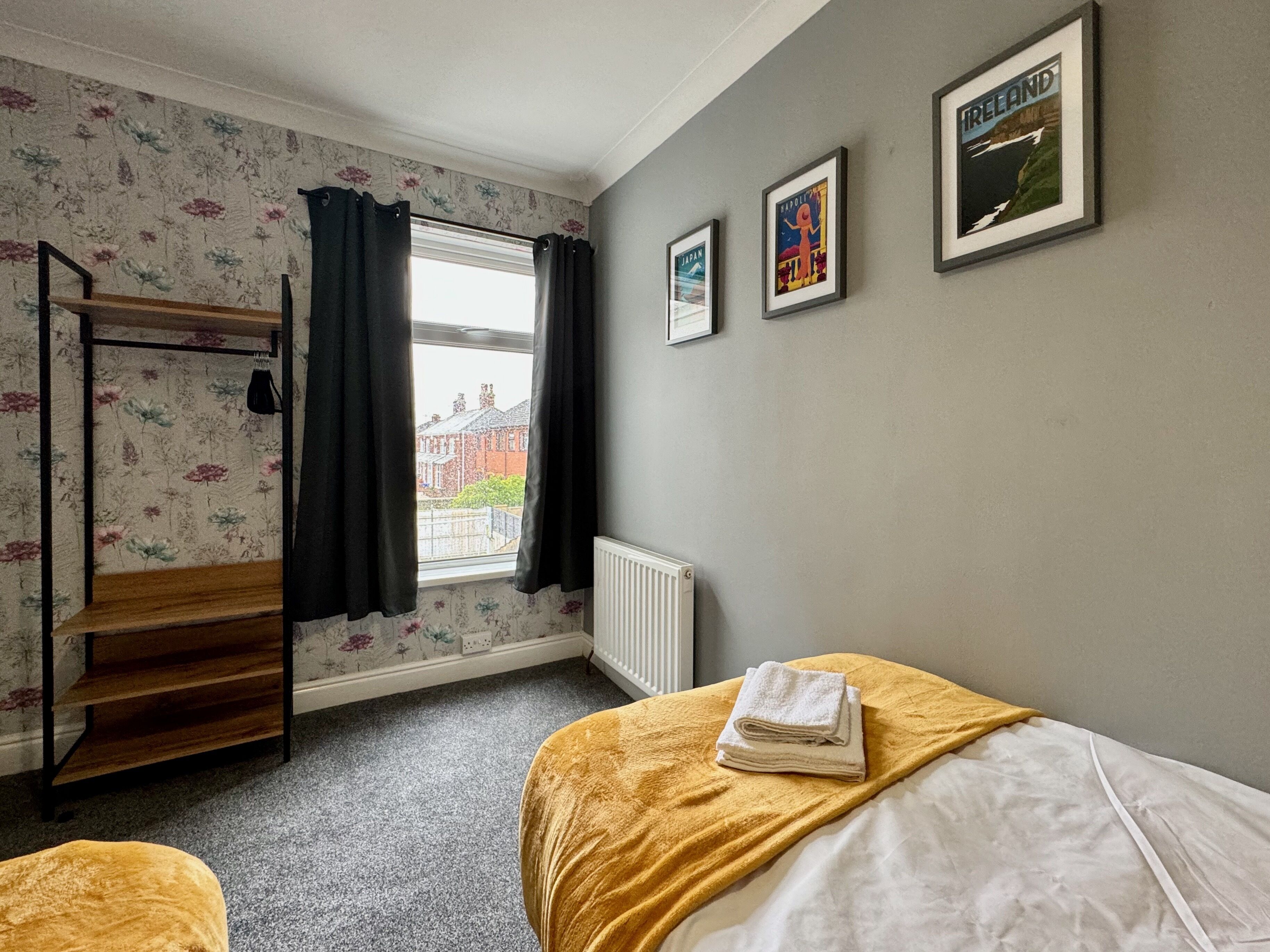 Une chambre avec un lit superposé, un radiateur, une fenêtre avec des rideaux et des tableaux encadrés accrochés au mur.