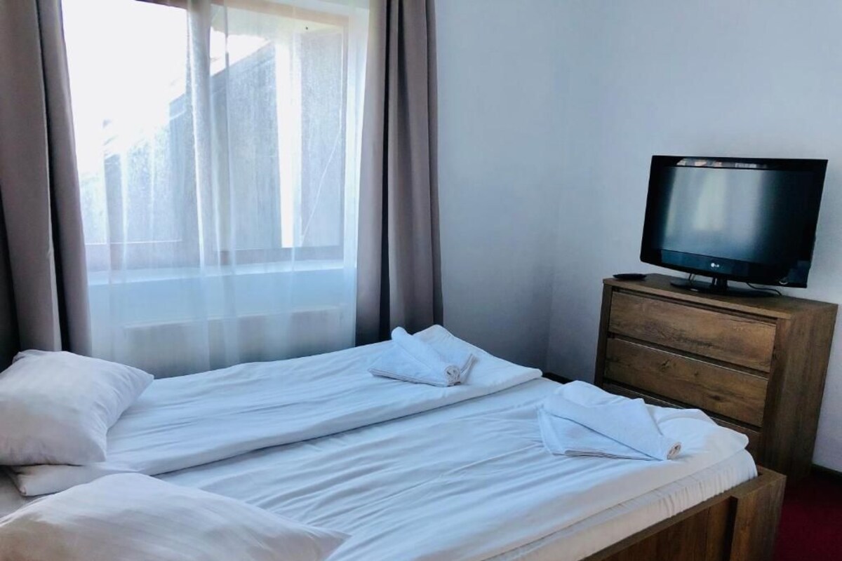 Habitación de hotel con cama, televisor sobre un aparador de madera y ventana con cortinas.