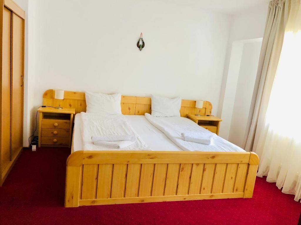 A double bed with wooden headboard and footboard, two bedside tables, a wall-mounted light, and a red carpeted floor.