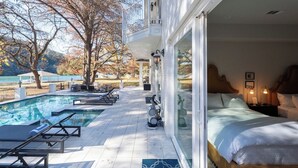 Habitació d'hotel amb un llit gran, vistes a una piscina i un balcó que s'obre a una zona enjardinada.