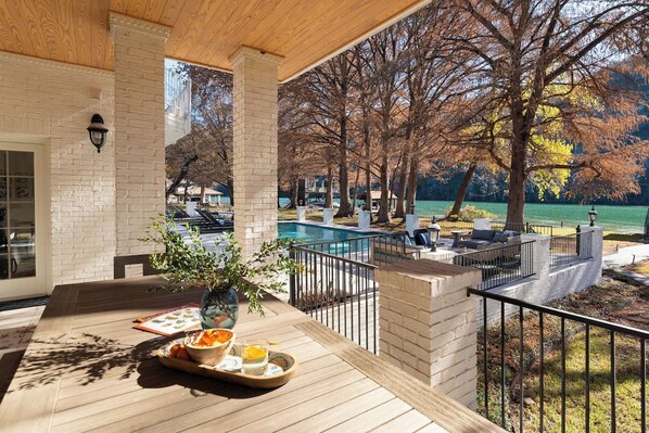 Un espacio exterior techado con piscina, sillas de descanso y una mesa de comedor con una bandeja de comida.