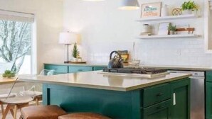 Een moderne keuken met een centraal eiland, groene keukenkastjes en hanglampen.