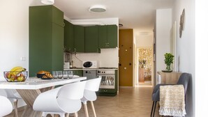 A modern kitchen with green cabinets, a white countertop, and a dining area with white chairs.