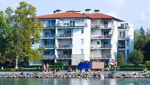 A multi-story residential building with balconies, located near a body of water.
