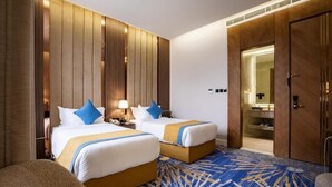A hotel room with two beds, a sitting area, a bathroom with a mirror, and a patterned carpet. - Novo Hotel Riyadh (Riyadh)