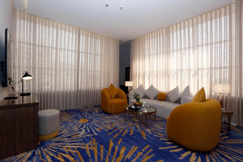 Une chambre d’hôtel moderne dotée d’une grande fenêtre, d’un canapé, d’un fauteuil, d’une table basse et d’un tapis décoratif.
