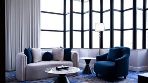 A modern hotel room with a large window, a sofa, a chair, a small table, and a lamp. - Novo Hotel Riyadh (Riyadh)