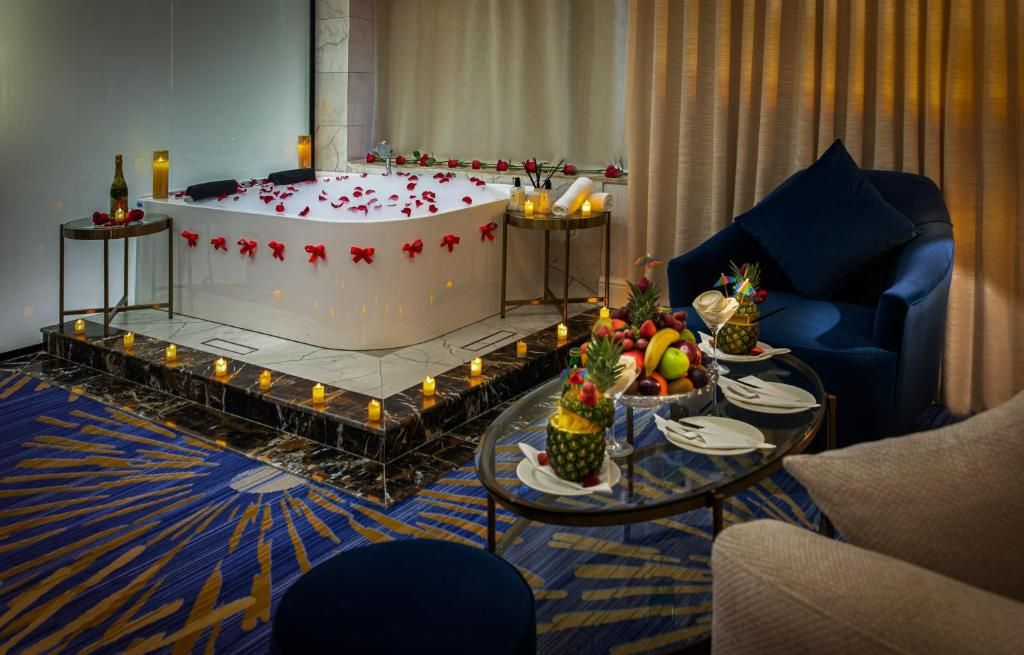 A luxurious room with a large bathtub, a dining table with fruit, and a blue sofa.