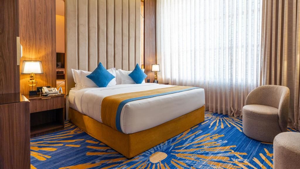 Une chambre d’hôtel avec un grand lit, deux lampes de chevet, une table de chevet en bois, une chaise et une moquette à motifs.