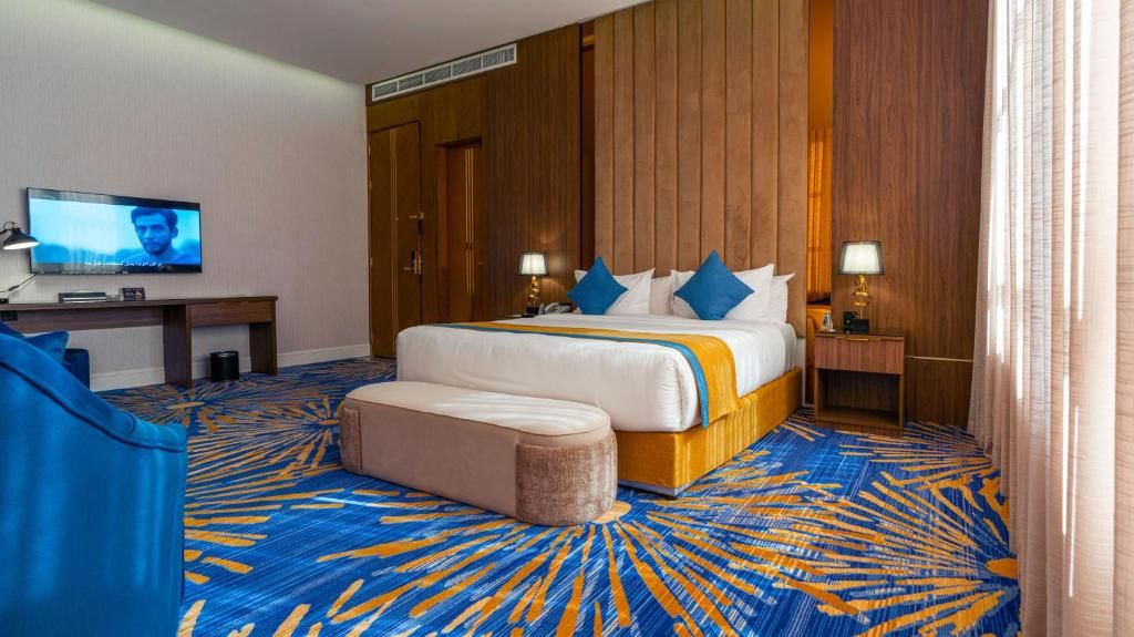 A hotel room with a large bed, a desk, a television, and a patterned carpet.
