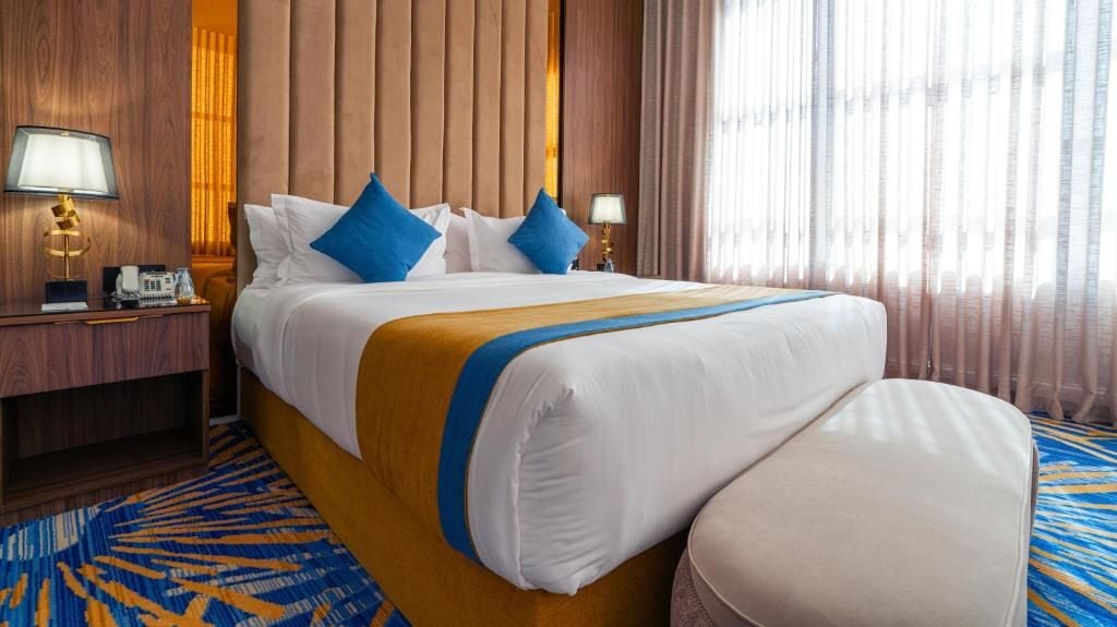 Een hotelkamer met een groot bed, twee nachtkastjes, een lamp en een kamerbreed tapijt met dessin.