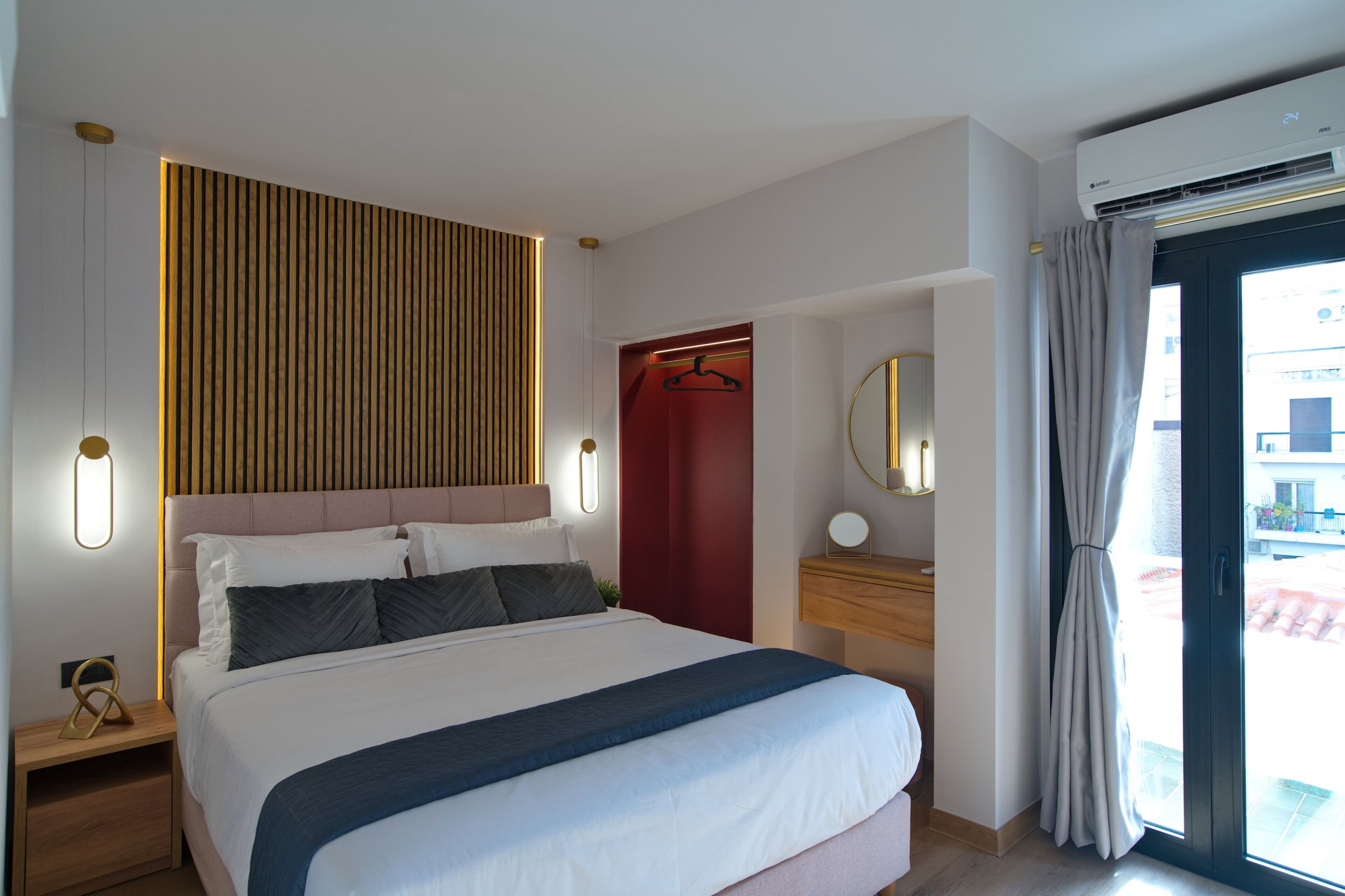 Quarto de hotel moderno com uma cama grande, mesas de cabeceira, um espelho e vista através de uma porta de vidro deslizante.