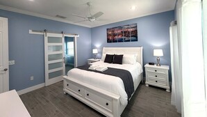 A bedroom with a bed, nightstands, a ceiling fan, a painting, and a sliding door.