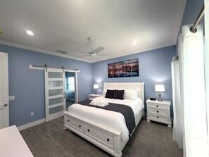 A bedroom with a bed, nightstands, a ceiling fan, a painting, and a sliding door. - BRAND NEW! Lakefront 9BR Pool Hot Tub Outdoor Kitchen BBQ Theater 2 miles Disney (Kissimmee)