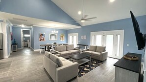 A spacious living room with a dining area, a kitchen, and a TV mounted on the wall.