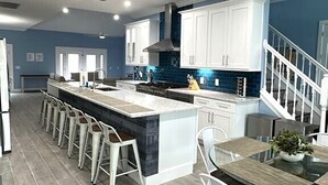 A modern kitchen with a central island, bar stools, and a dining table with chairs.