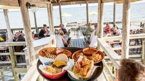 Eine Holzterrasse mit Tischen und Stühlen mit Blick auf ein Gewässer.