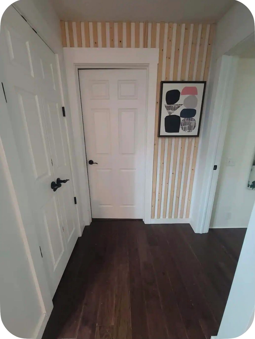 Un couloir avec un plancher en bois, une porte blanche et un mur à rayures.