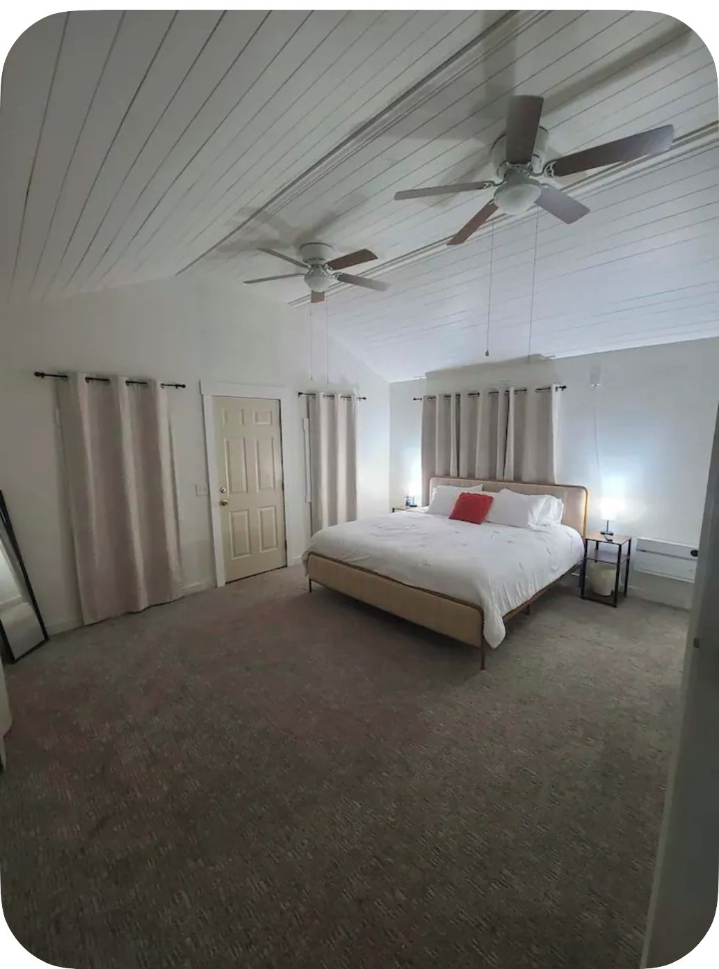 A bedroom with a bed, two ceiling fans, a nightstand, and a window with curtains.