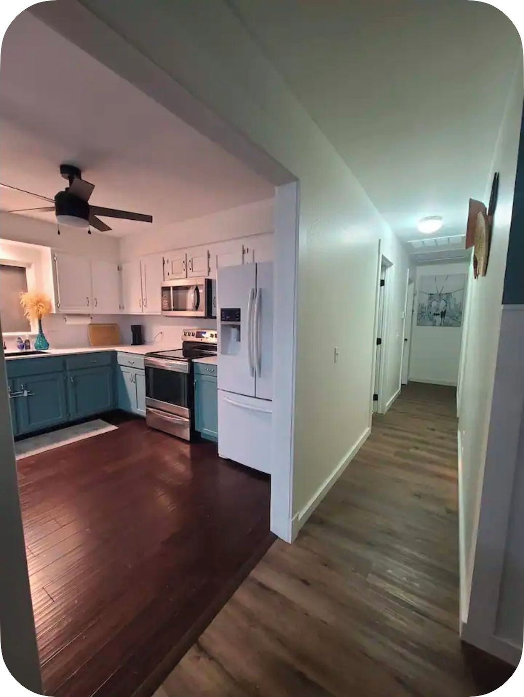A modern kitchen with white cabinets, a microwave, a refrigerator, and a ceiling fan.