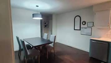 A dining area with a table and chairs, a pendant light, and a kitchen area with a refrigerator.