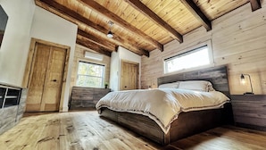 Un dormitorio con techo de madera, una cama grande, una mesita de noche y un ventanal.