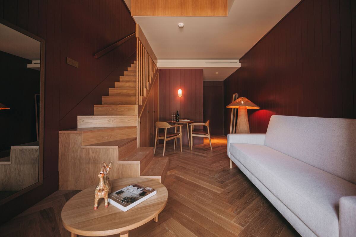 Una sala de estar moderna con una escalera de madera, un sofá, una mesa de centro redonda y un comedor.