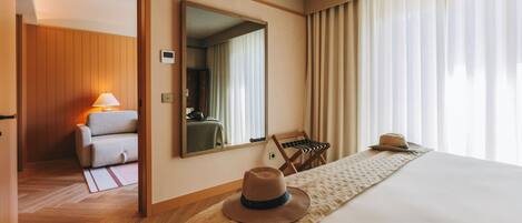 A hotel room with a bed, a mirror, a chair, and a hat on the bed.