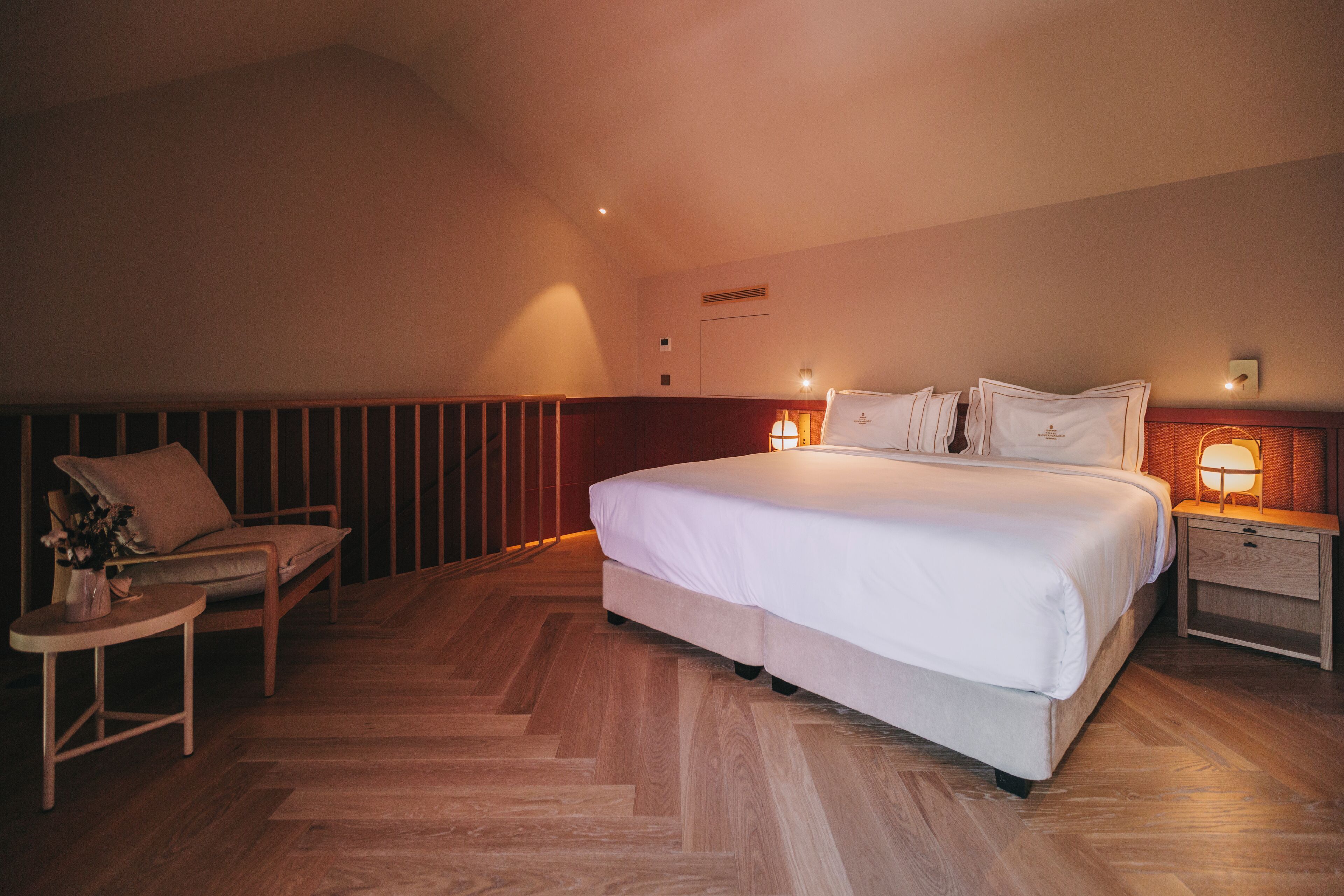 A bedroom with a large bed, bedside tables, a chair, and a small table with a vase of flowers.