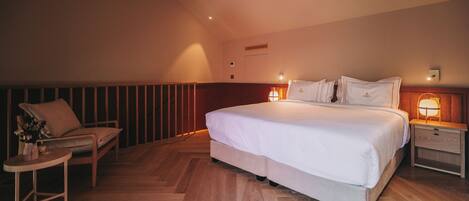 A bedroom with a large bed, bedside tables, a chair, and a small table with a vase of flowers.