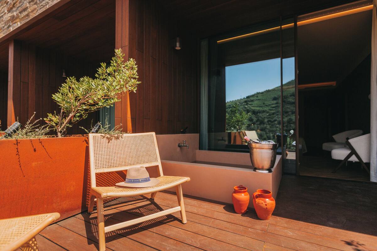 Una terraza de madera con una silla de mimbre, dos jarrones anaranjados y una planta en maceta.