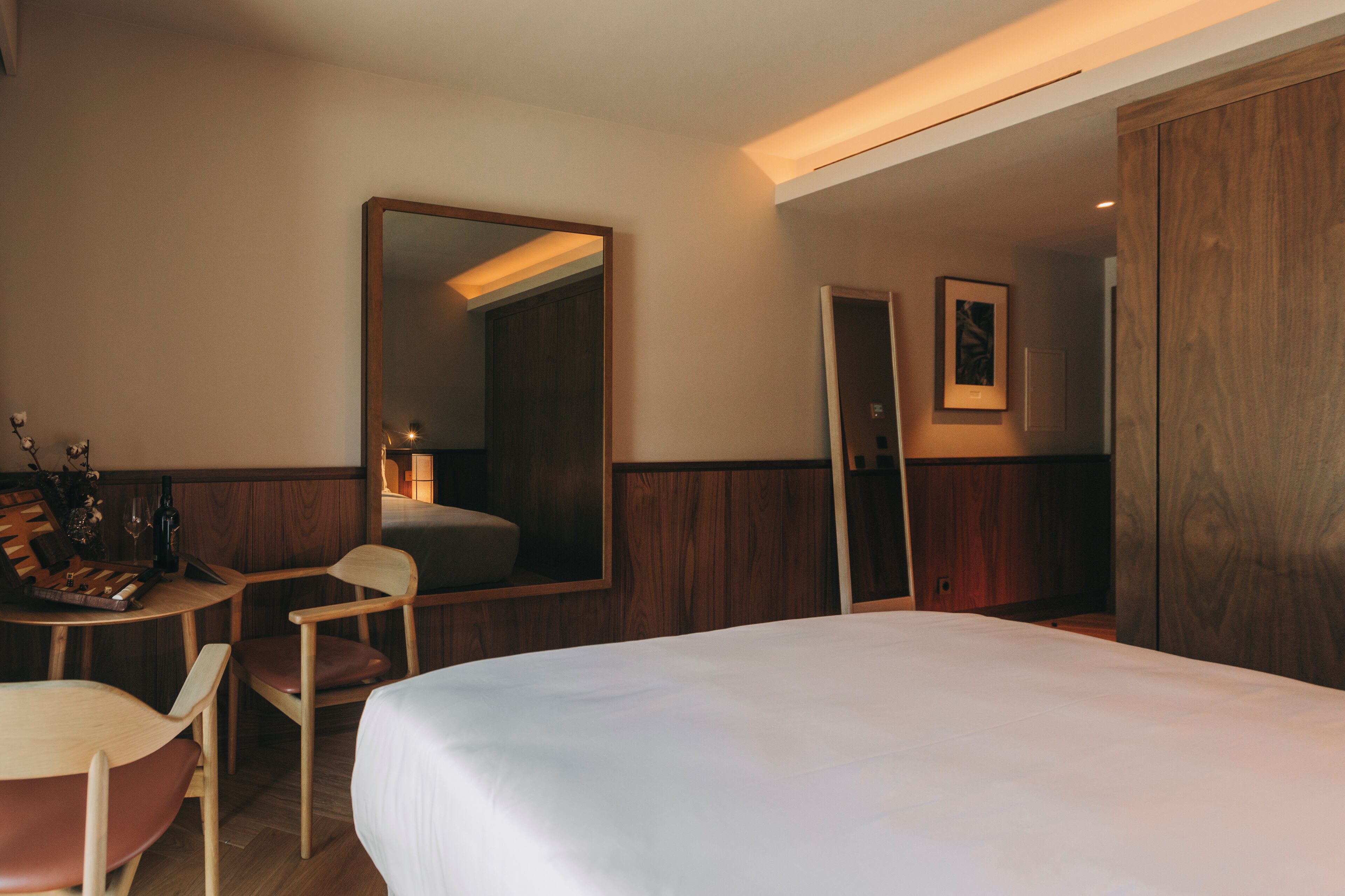 A hotel room with a large bed, a wooden desk, a chair, a mirror, and a wardrobe.