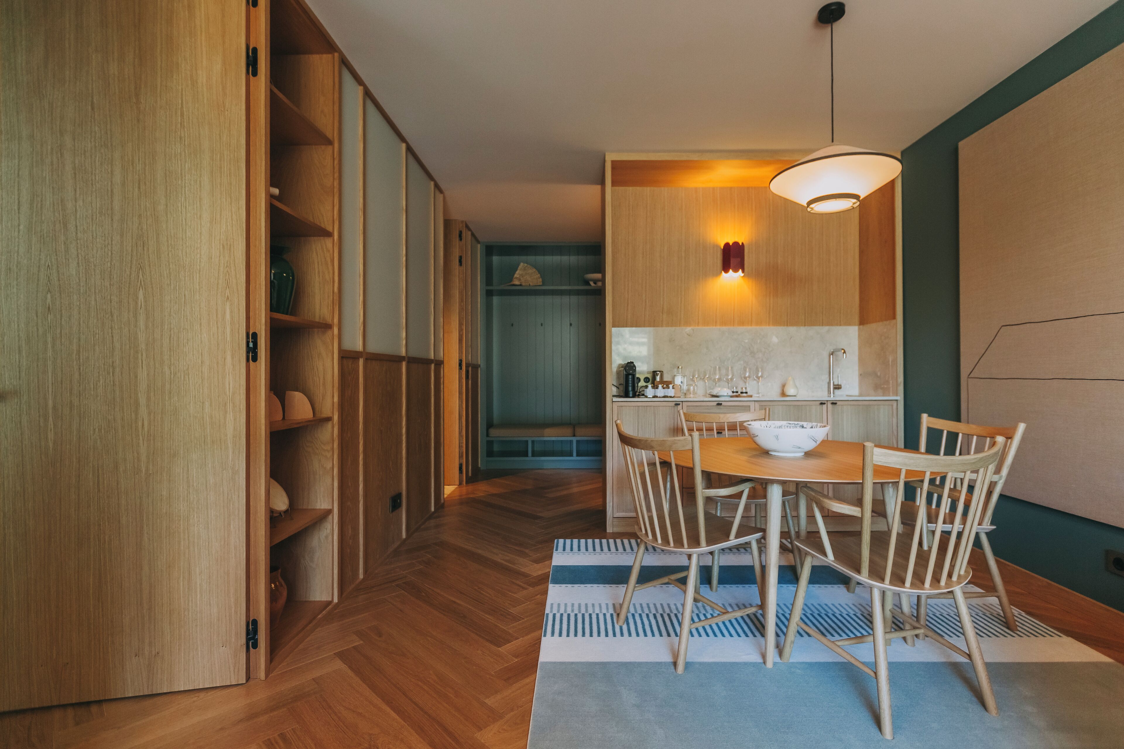 A modern kitchen with wooden cabinets, a dining table with chairs, and a hanging light fixture.