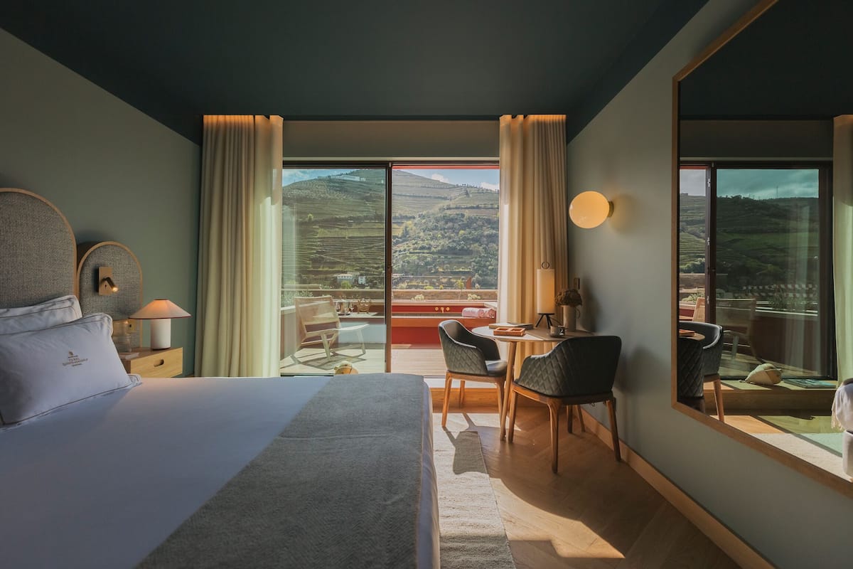 Habitación de hotel con una cama grande, un escritorio y vistas al campo a través de amplios ventanales.