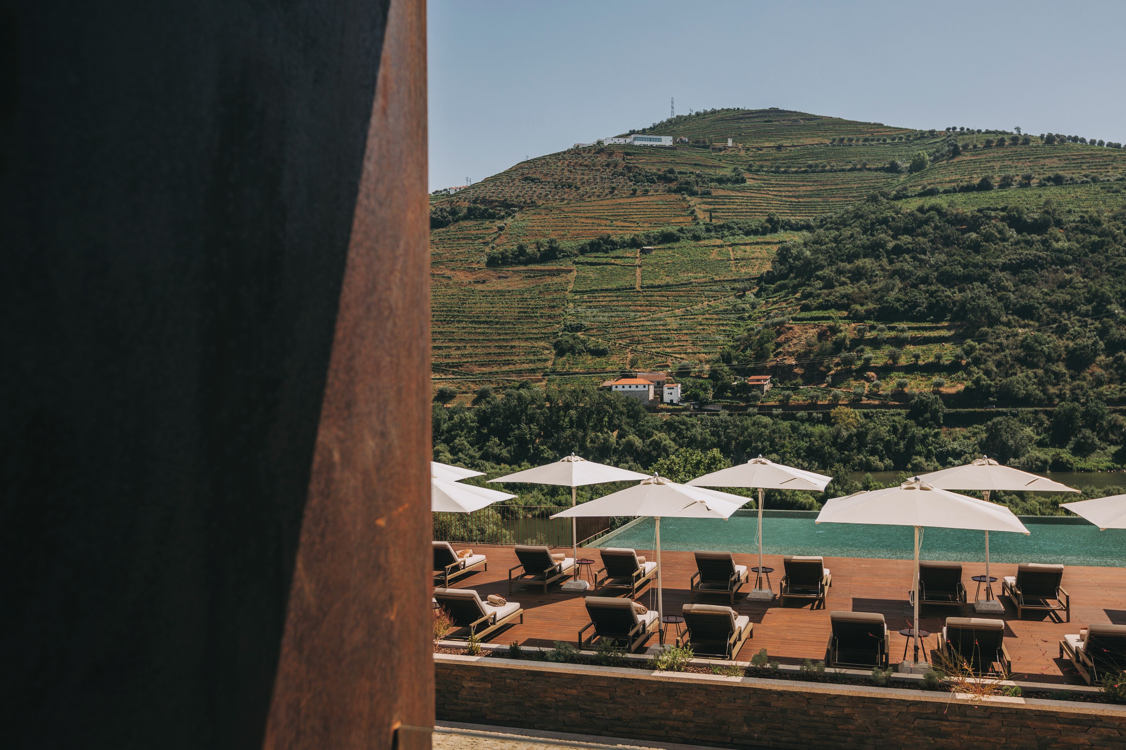 A terrace with sun loungers and umbrellas overlooking a vineyard and a hill.