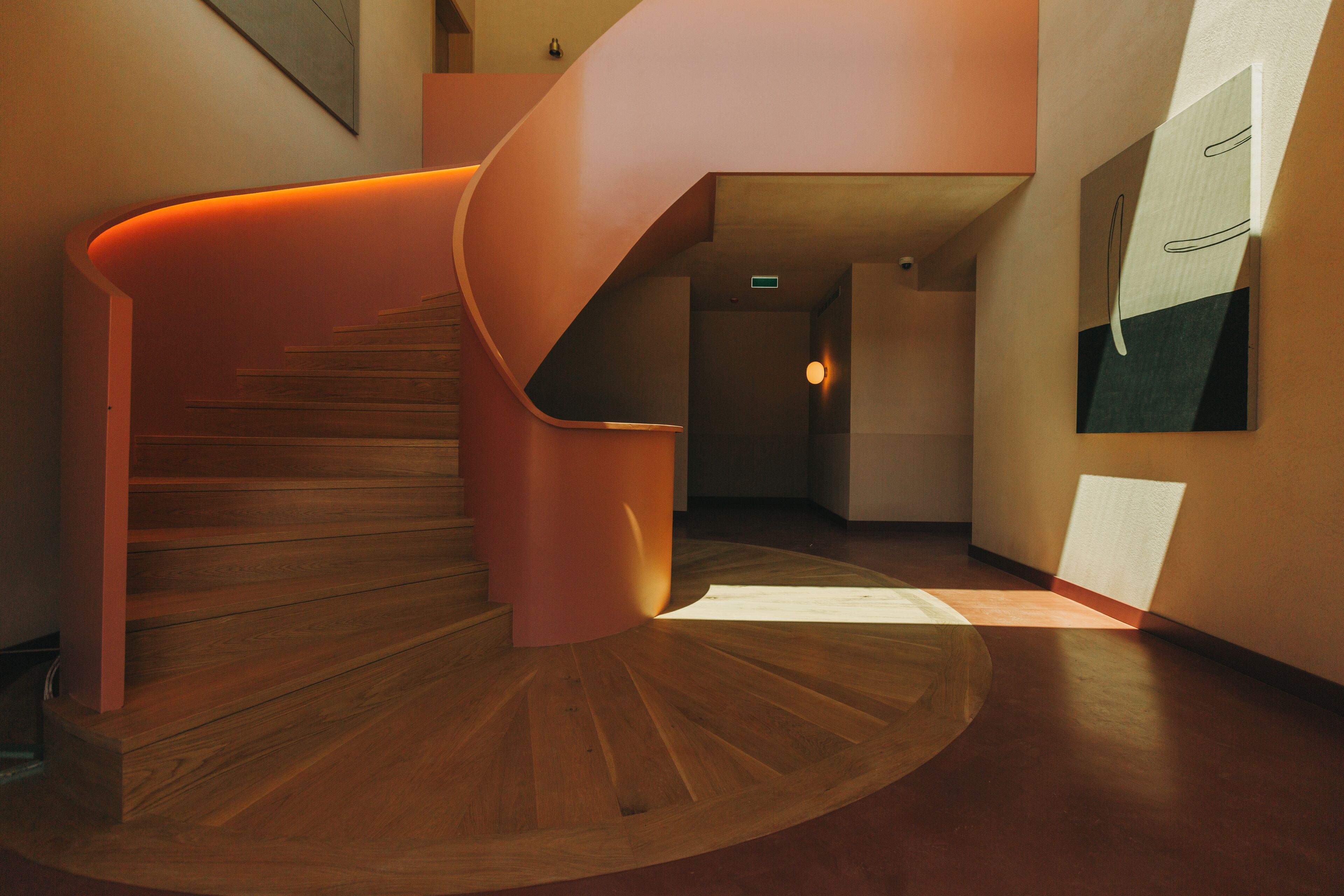 Una escalera en espiral moderna con escalones de madera y barandilla curva, que conduce a una zona de descanso con una lámpara.