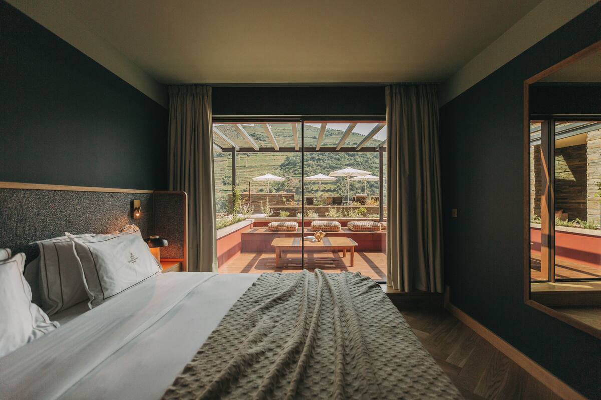 Habitación de hotel con una cama grande, vistas al área de estar exterior a través de una puerta de cristal y suelo de madera.