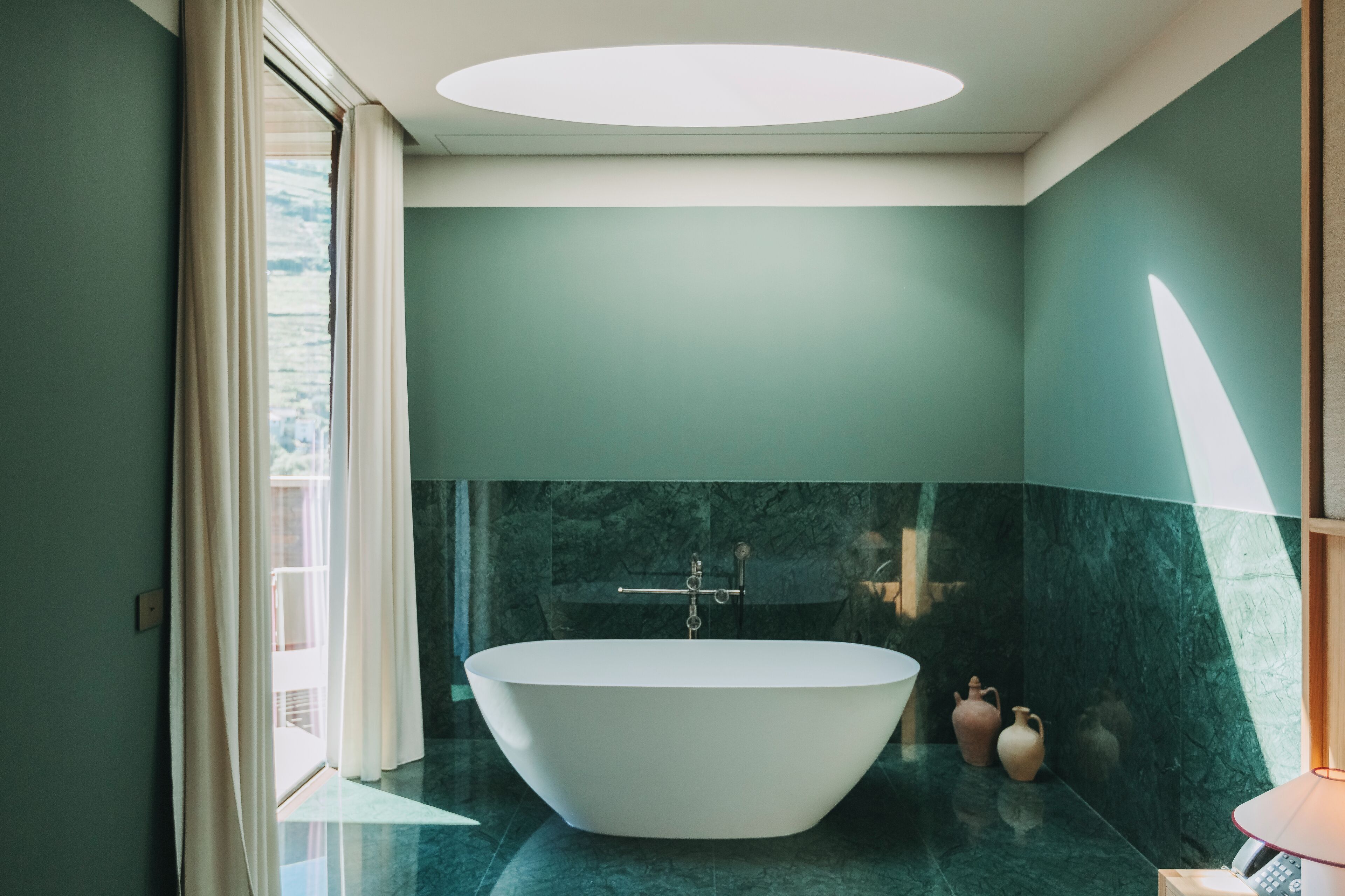 A modern bathroom with a freestanding bathtub, marble walls, and a skylight.