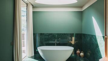 A modern bathroom with a freestanding bathtub, marble walls, and a skylight.