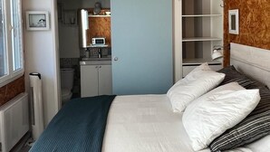 A bedroom with a bed, a wardrobe, and a bathroom visible through an open door. - Cabane Edena, Terrasse Ombragée Jardin Vélos Wifi à 350m de la Plage du Mauret (Andernos-les-Bains)