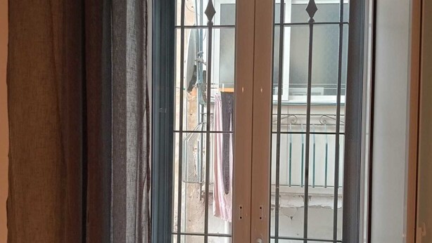 Habitación con una ventana grande que tiene barrotes y vista a un balcón con ropa tendida.