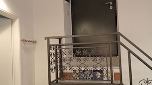 Una escalera con una puerta negra, barandilla metálica y una mesita con mantel verde.