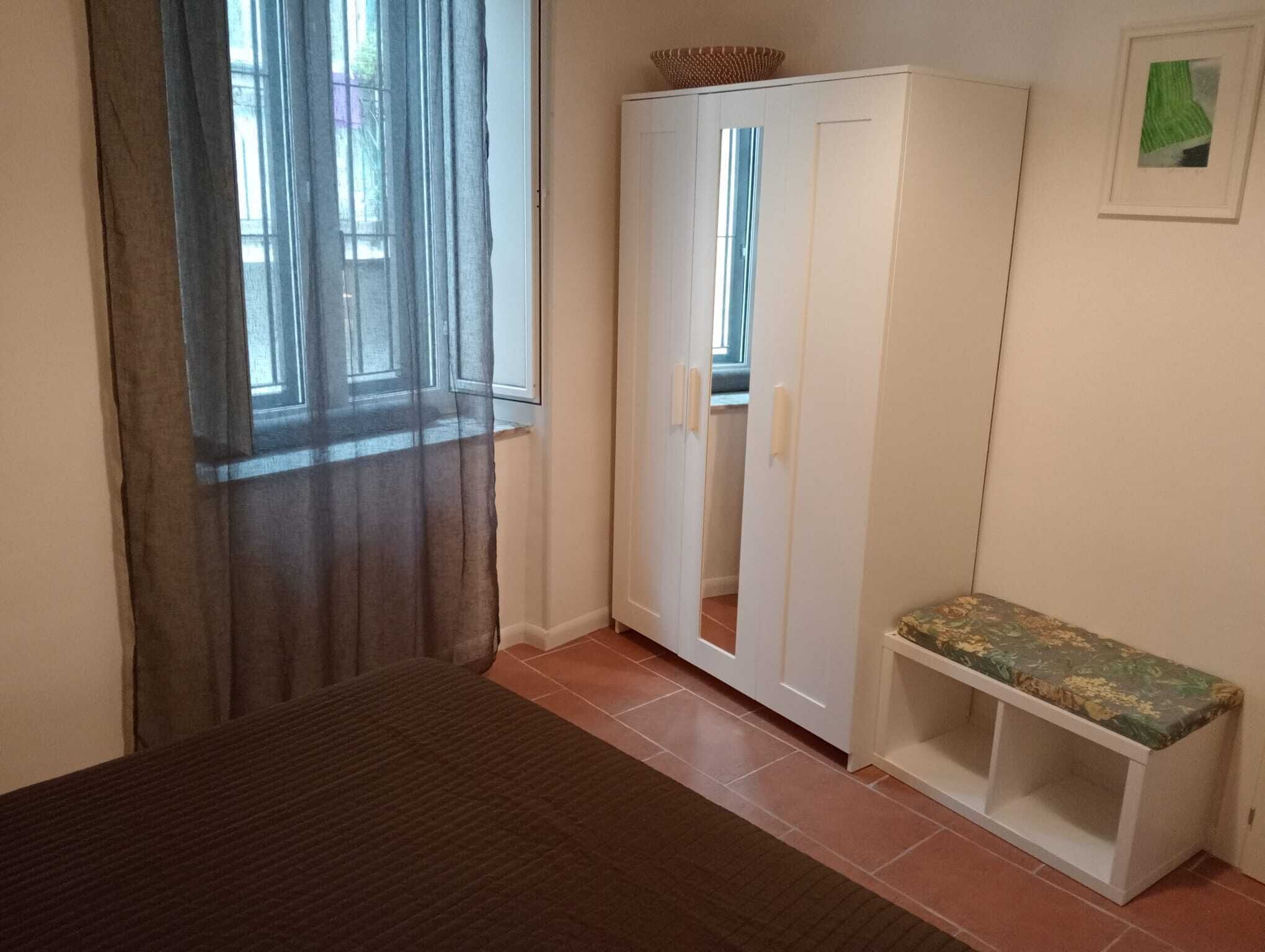 Ein Schlafzimmer mit Bett, Kleiderschrank, einer Bank und einem Fenster mit Vorhängen.