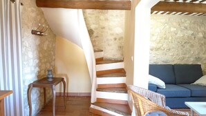 A rustic interior with a spiral staircase, a wicker chair, a blue sofa, and a small table. - Charme D'un mas en Luberon, Calme, vue Panoramique, Piscine, Cheminée (Lacoste)