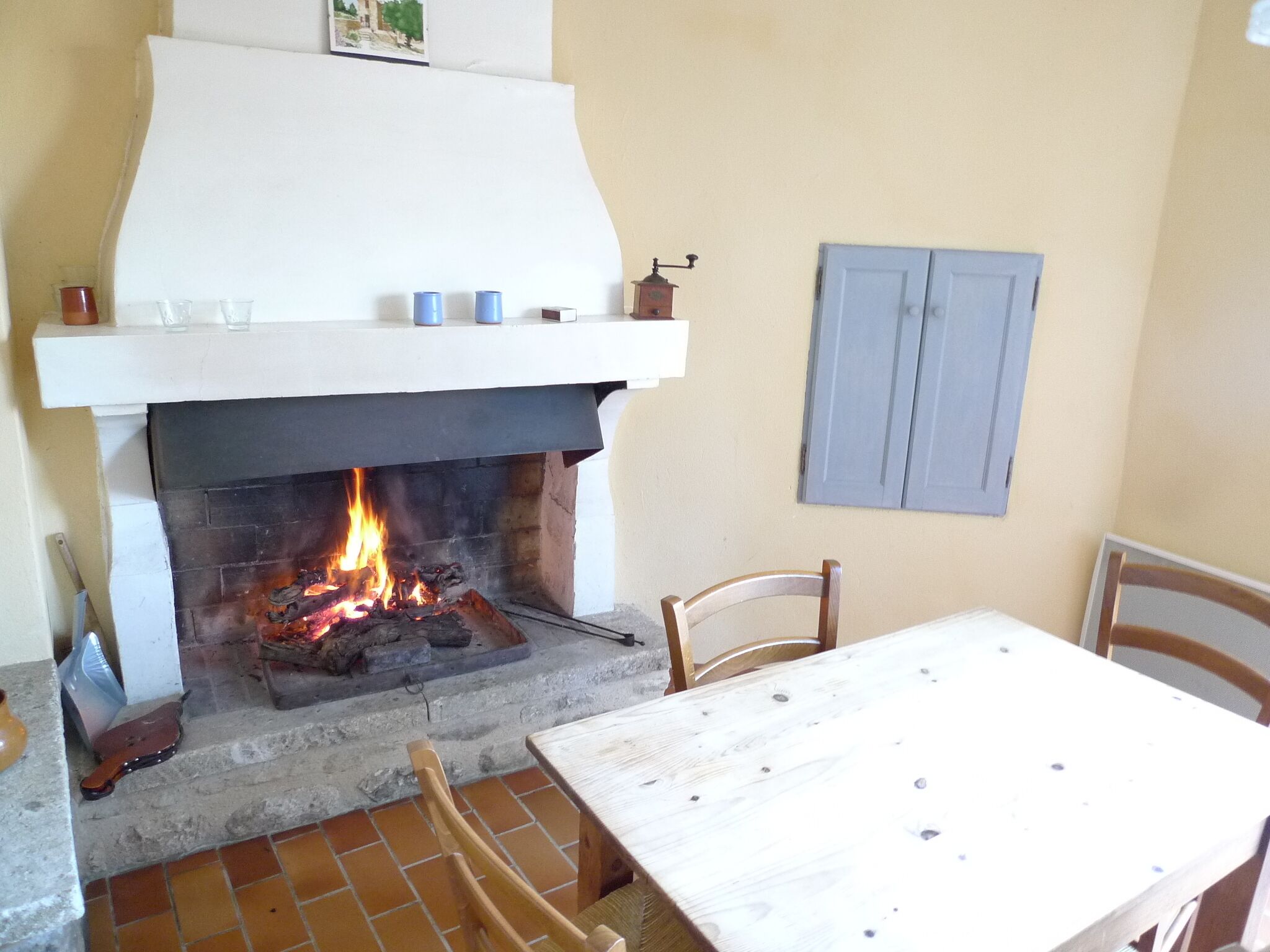 A fireplace with a fire, a white mantel, and a table with chairs.