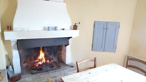 A fireplace with a fire, a white mantel, and a table with chairs. - Charme D'un mas en Luberon, Calme, vue Panoramique, Piscine, Cheminée (Lacoste)