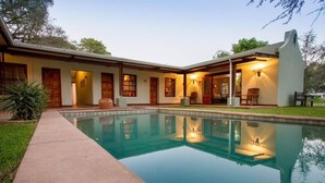 A house with a swimming pool, wooden doors, and a patio area with chairs. - Thorn Tree House (Livingstone)