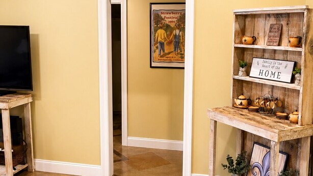 A hallway with a television on the left, a framed picture on the wall, and a wooden shelf with decorative items on the right. - Cozy Cajun

 (Ponchatoula)