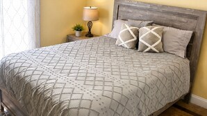 A bedroom with a bed, a ceiling fan, a nightstand with a lamp, and a window with curtains. - Cozy Cajun

 (Ponchatoula)