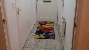 Un couloir étroit avec une porte blanche, un tapis coloré et un sol carrelé.